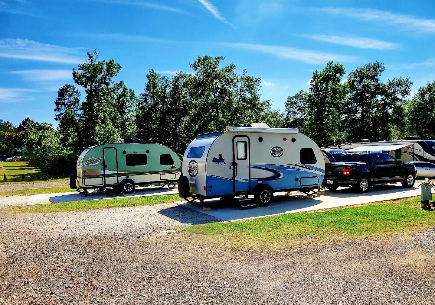 Two camper trailers on concrete pads under tall pines at Timberline RV Park