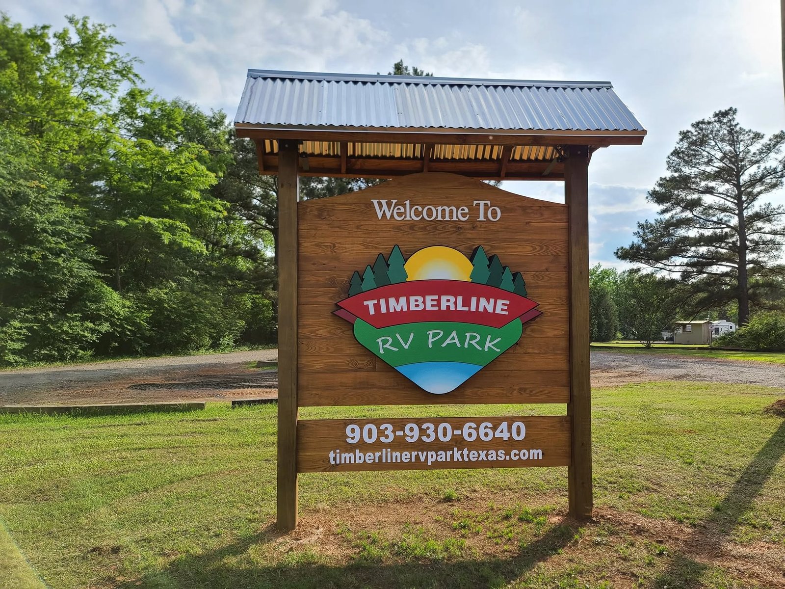 Wooden Welcome to Timberline RV Park entrance sign with the park logo, framed by pine trees